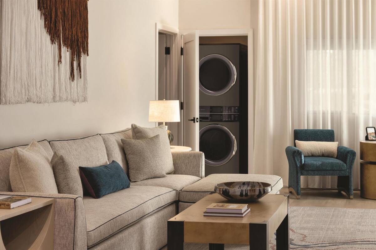 A living room with a sofa, a coffee table, a chair, a lamp, and a washing machine.