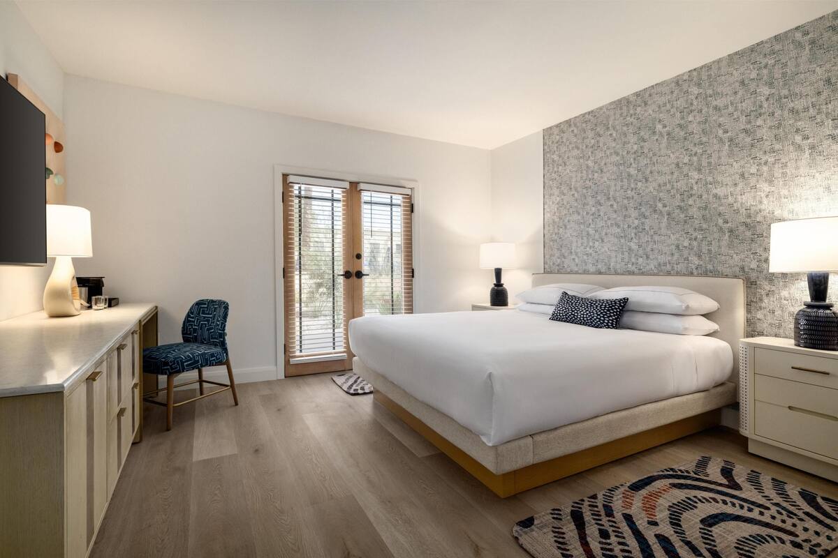 A bedroom with a bed, bedside tables, a chair, a desk, and a window with blinds.