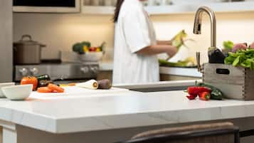 A kitchen with a countertop, a cutting board, vegetables, and a person preparing food.