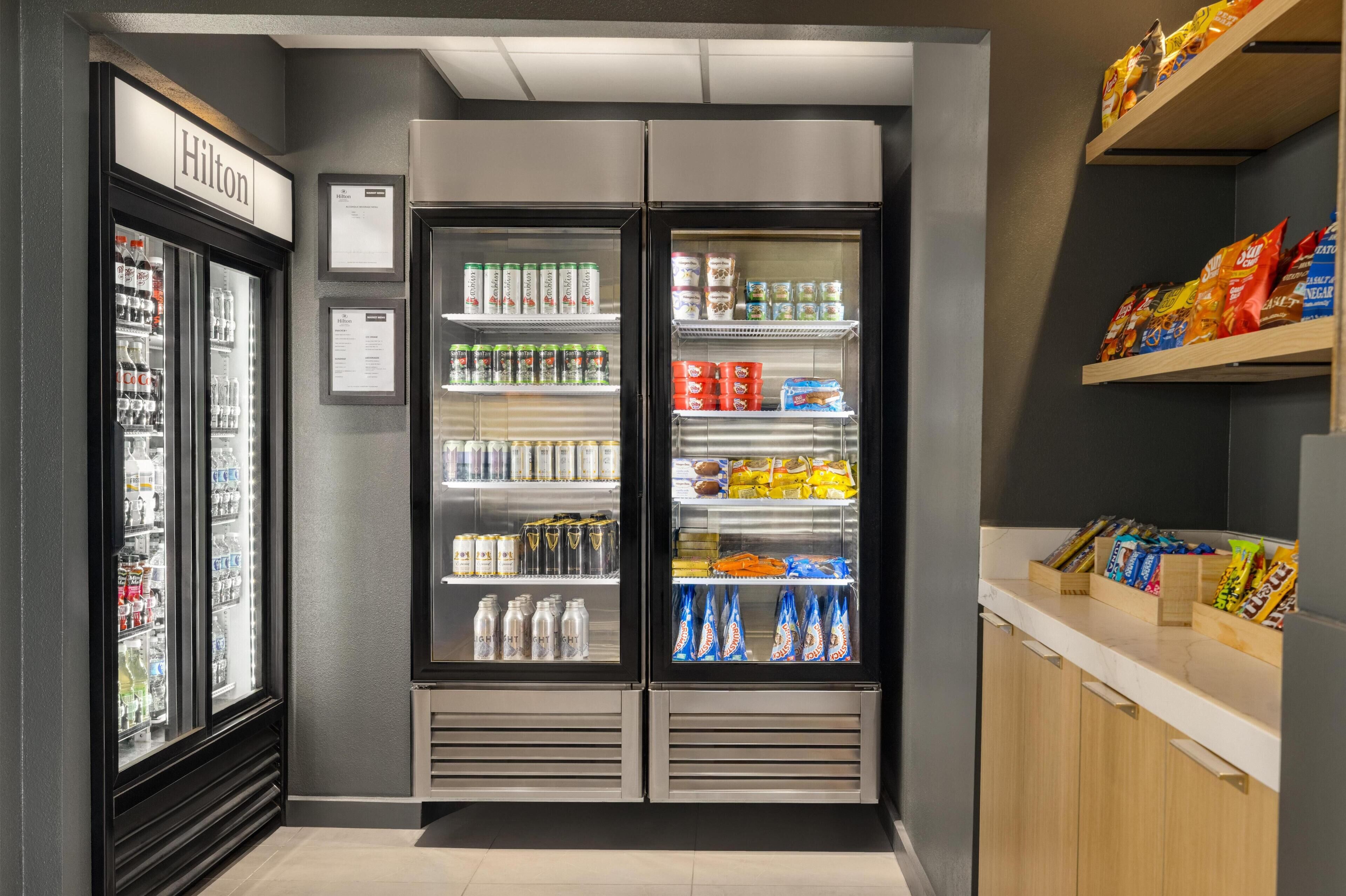 Eine Minibar mit verschiedenen Getränken und Snacks, ein Minibar-Schild und ein Regal mit verpackten Waren.