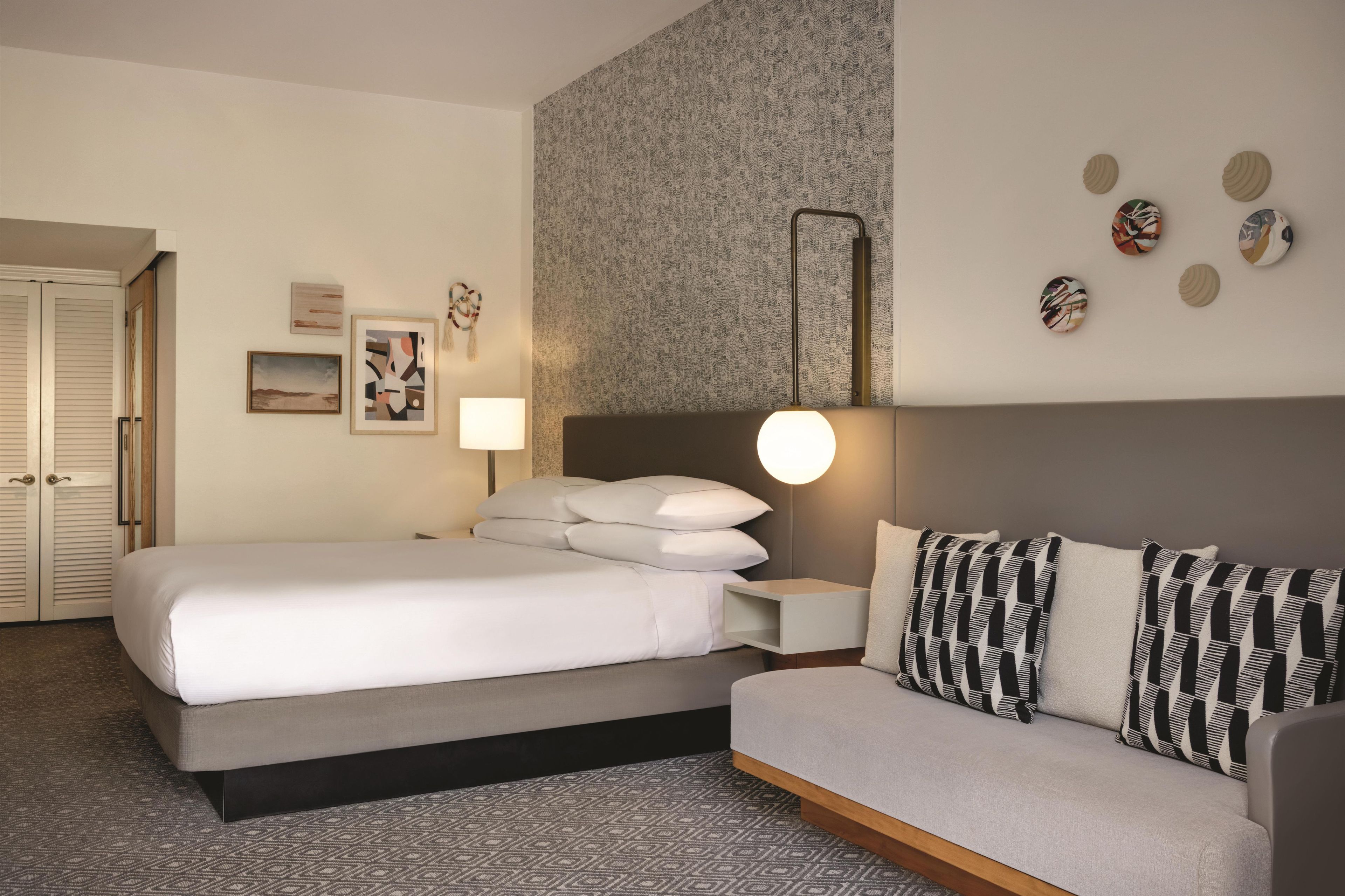 Una camera d'albergo con un letto, un divano, un comodino, una lampada e decorazioni alle pareti.