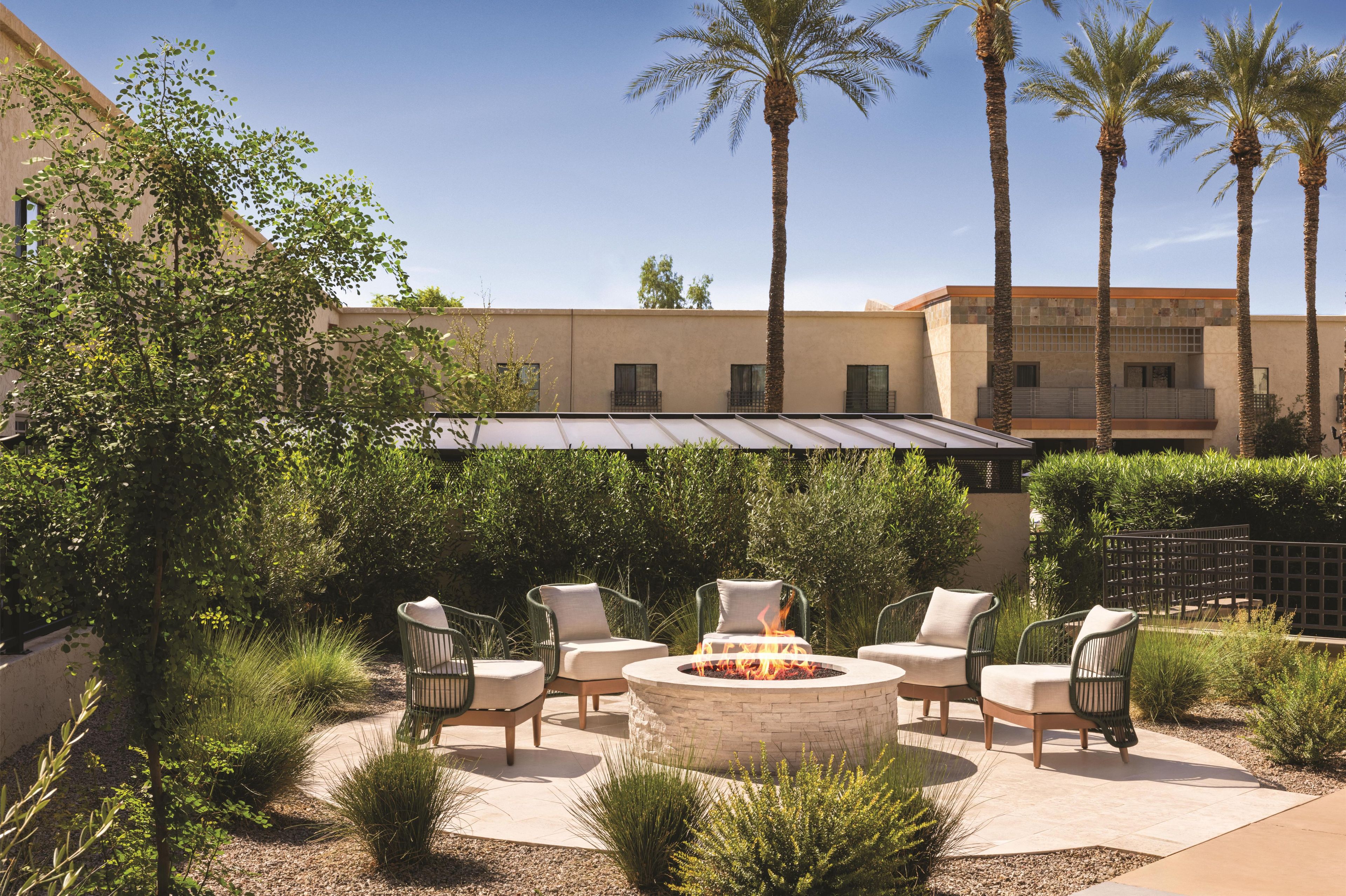 A courtyard with a fire pit, outdoor seating, palm trees, and a building in the background.