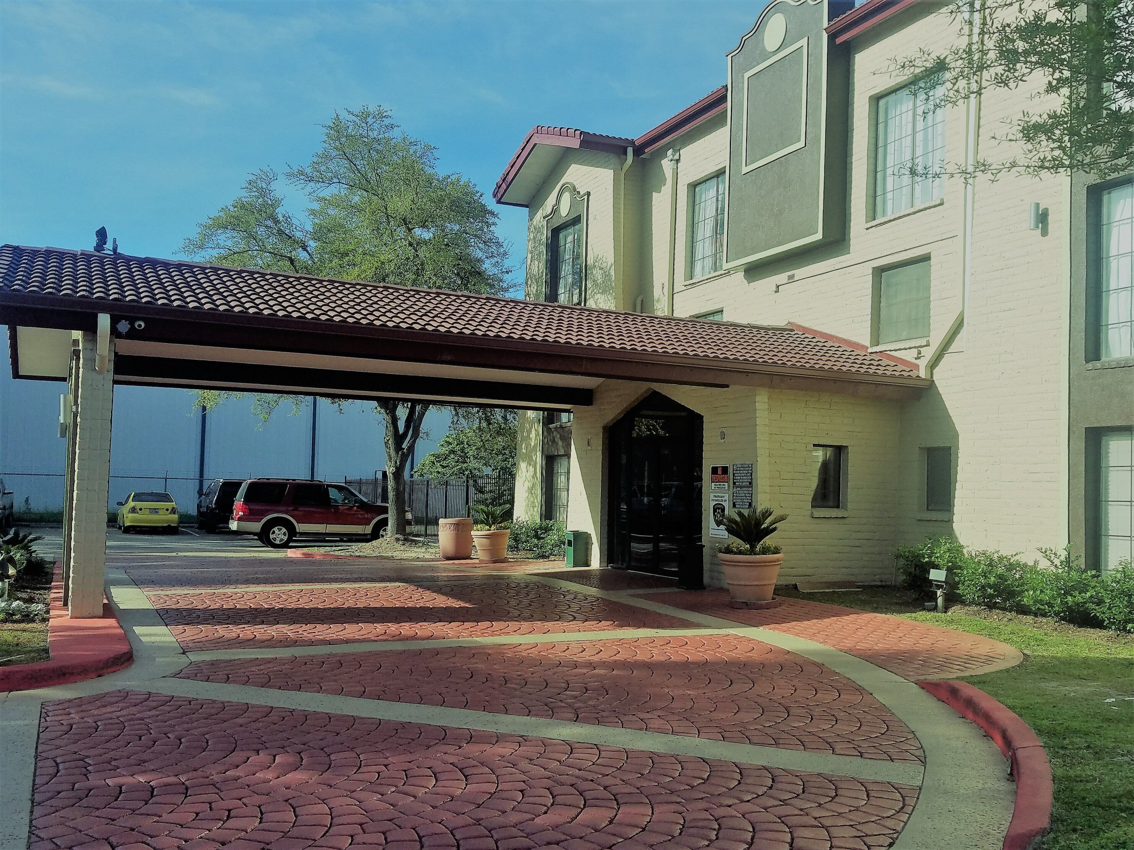 A building with a covered entrance, paved walkway, and parked cars.