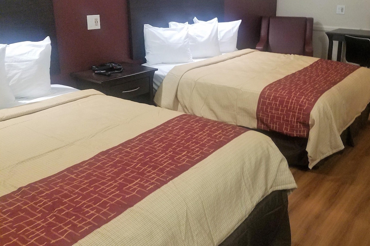 Two twin beds with beige and red bedspreads, a dark wooden nightstand, and a white wall socket.