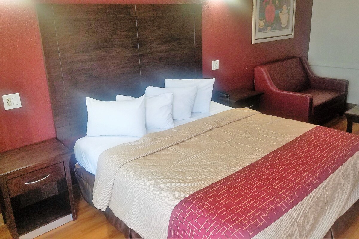 A hotel room with a bed, a nightstand, a chair, and a wall-mounted painting.