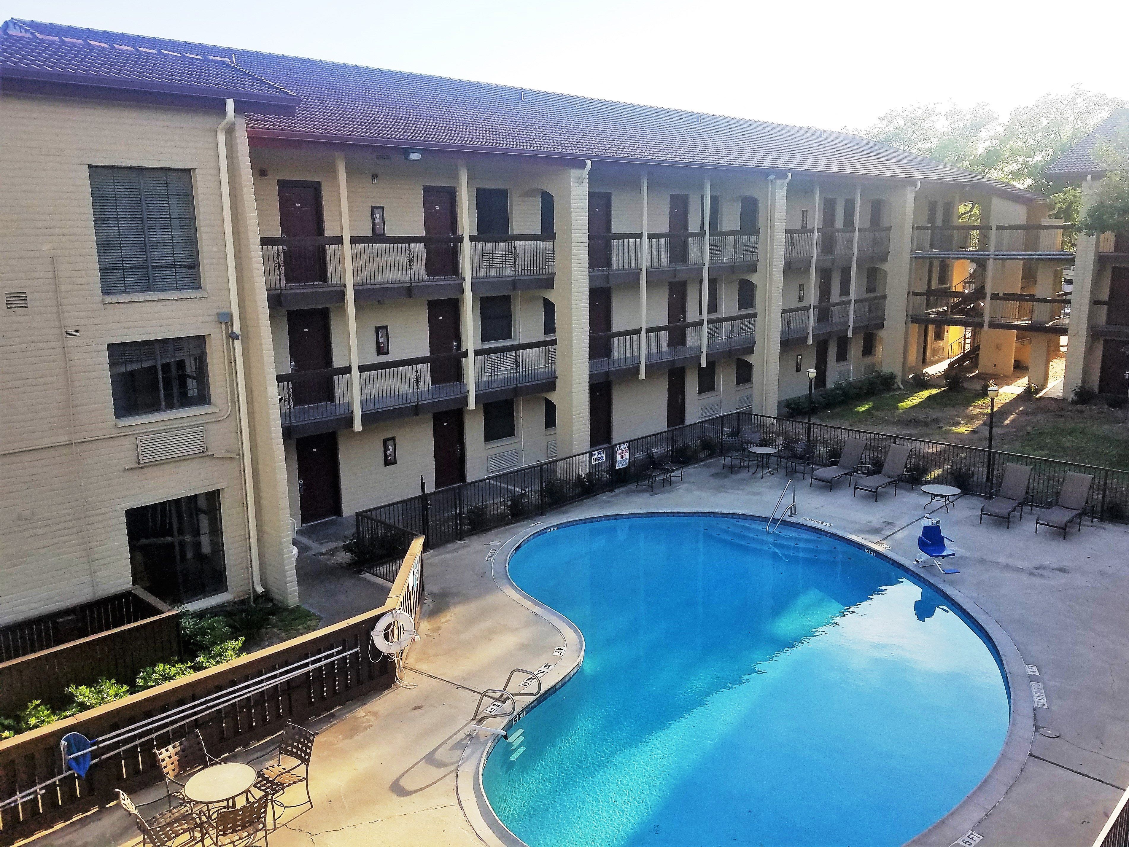 A multi-story building with a swimming pool, outdoor seating, and a fenced patio area.