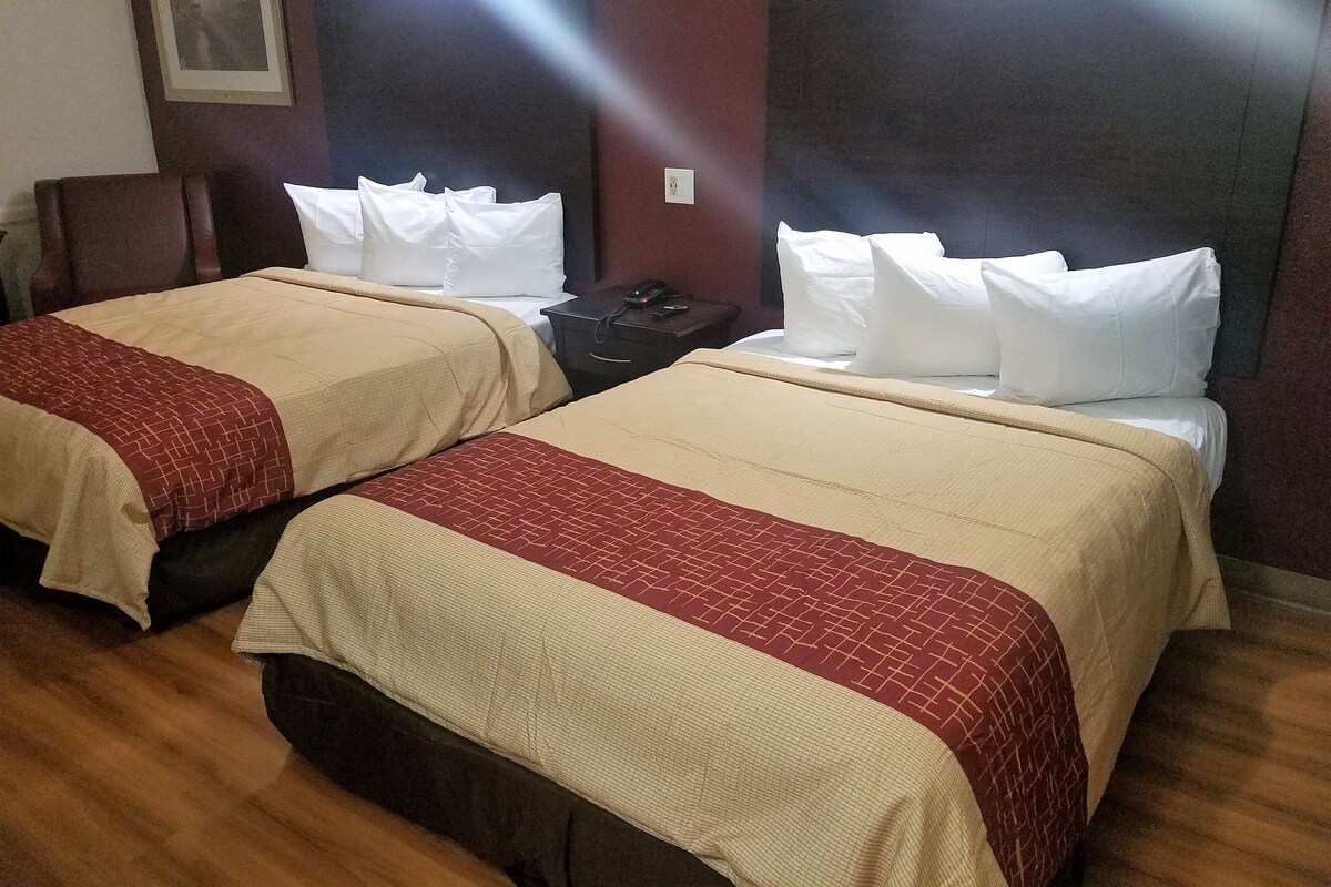 A hotel room with two beds, each with a headboard, a bedside table with a phone, and a wall-mounted light.