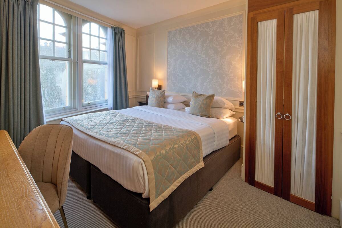 A neatly arranged hotel room with a large bed, a bedside table, a chair, and a wardrobe.