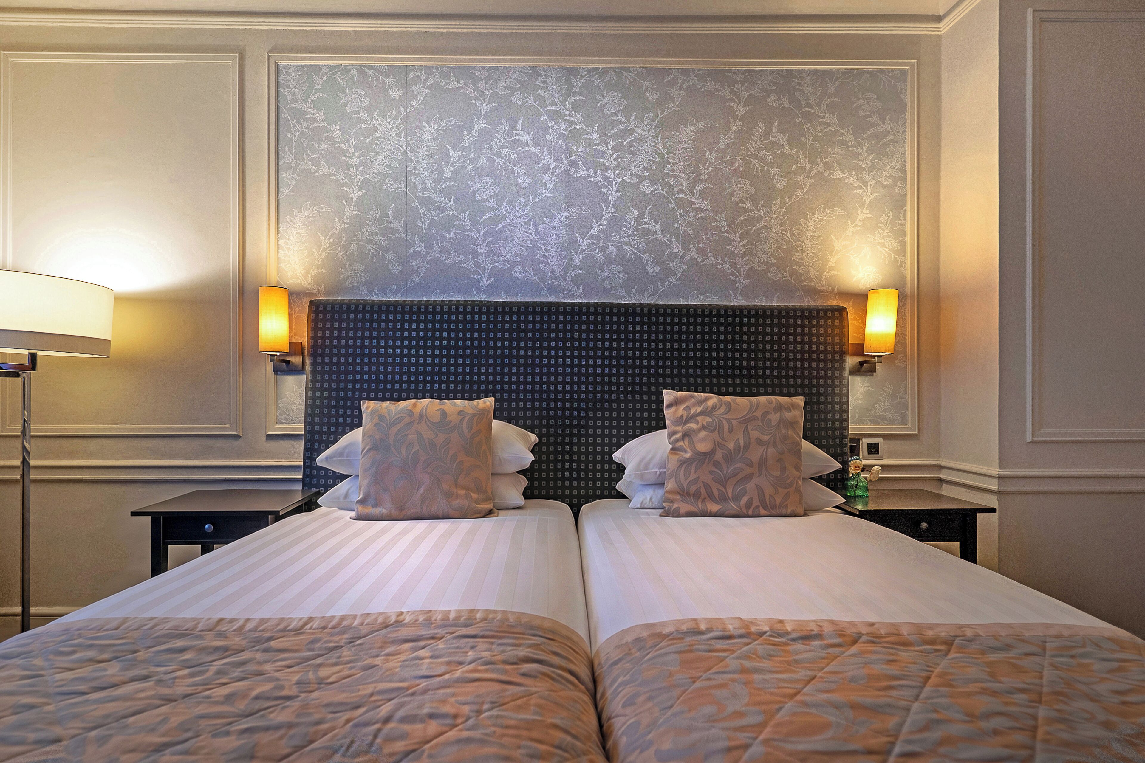 A hotel room with two beds, a large headboard, and two bedside lamps.