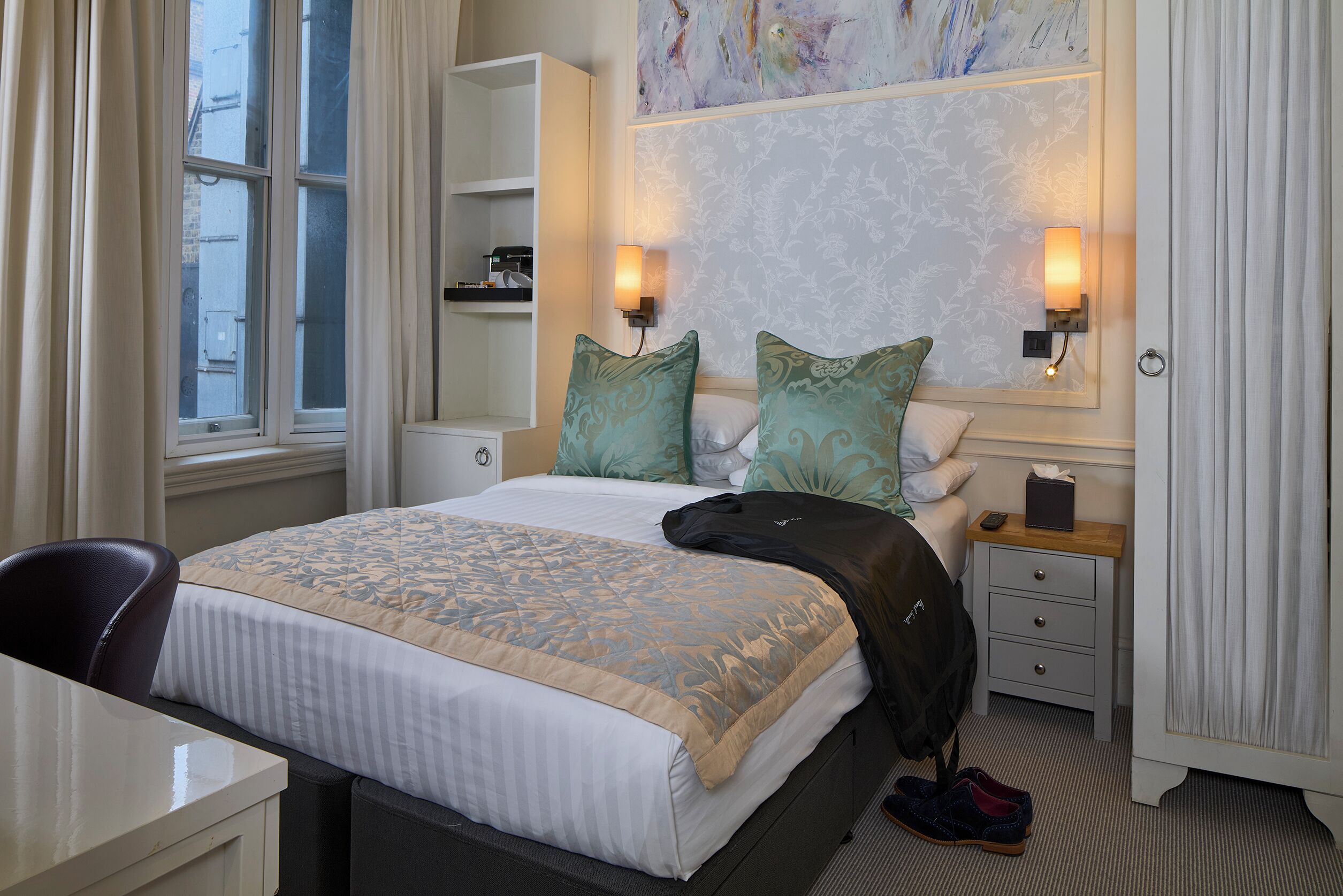 Ein Hotelzimmer mit Bett, Schreibtisch, Stuhl, Nachttisch, Lampe und einem Bild an der Wand.