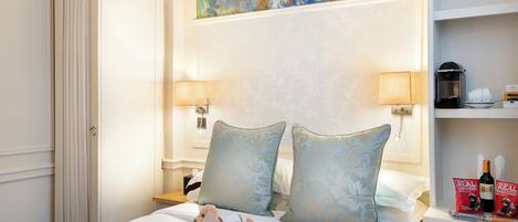 A hotel room with a bed, pillows, a nightstand, a lamp, a painting, and a stuffed toy.