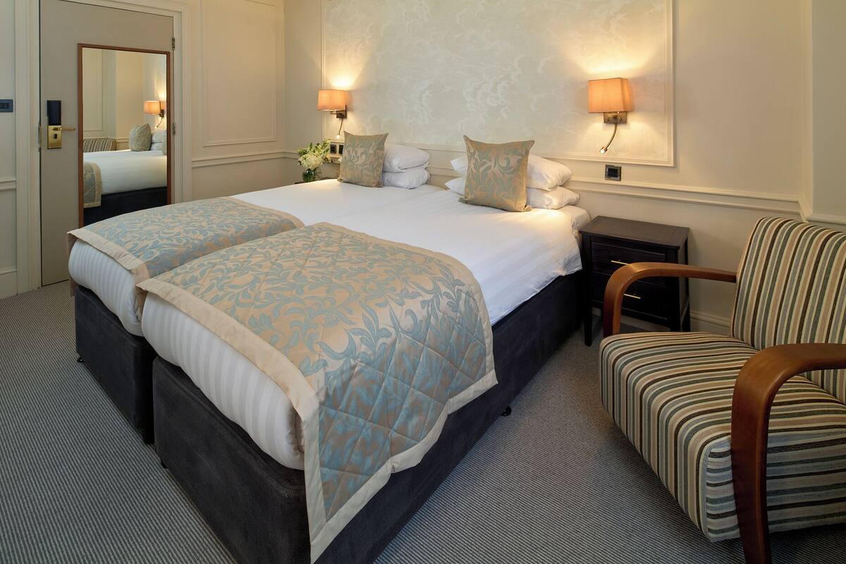 A hotel room with a large bed, two bedside tables, a chair, and a mirror.