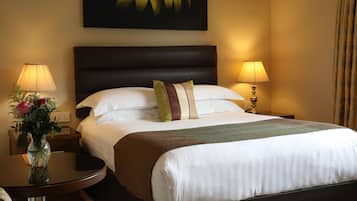 Habitación de hotel con una cama grande, dos lámparas de noche, un jarrón con flores y un cuadro en la pared.