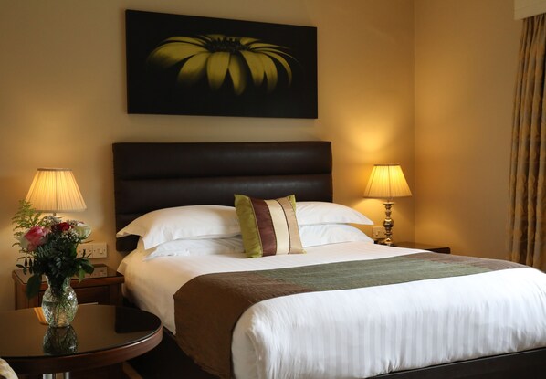 Habitación de hotel con una cama grande, dos lámparas de noche, un jarrón con flores y un cuadro en la pared.