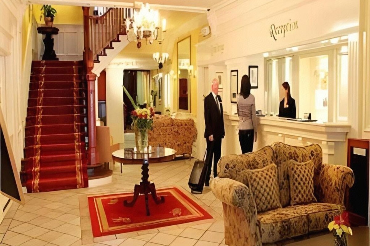 A hotel lobby with a staircase, a reception desk, a sofa, and a mirror.