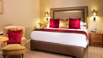 A hotel room with a large bed, a chair, a nightstand, and wall-mounted lamps.