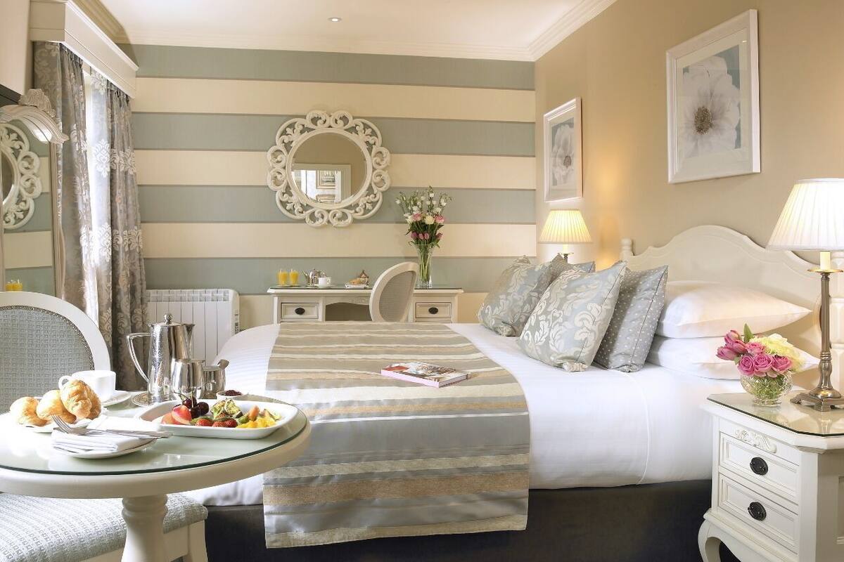 A hotel room with a bed, bedside tables, a round table with breakfast, and a mirror.