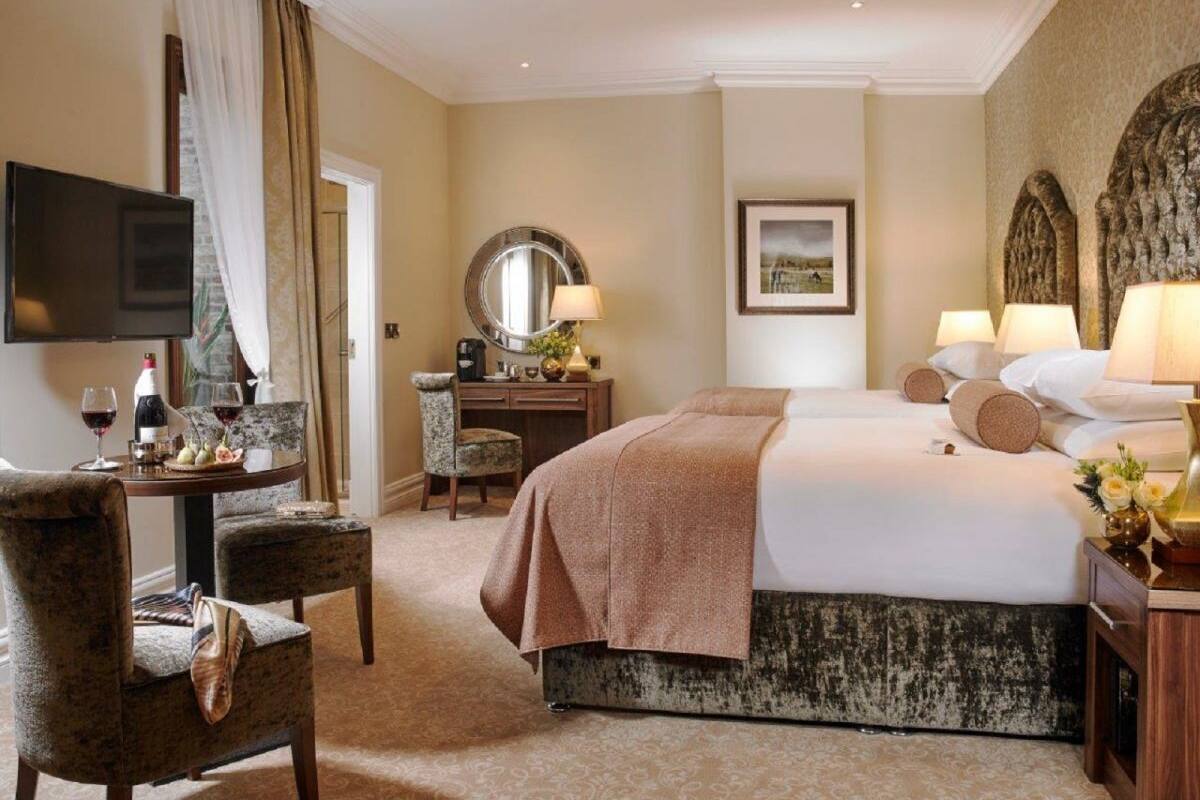 A hotel room with a bed, a desk with a chair, a television, and a dining table with chairs.