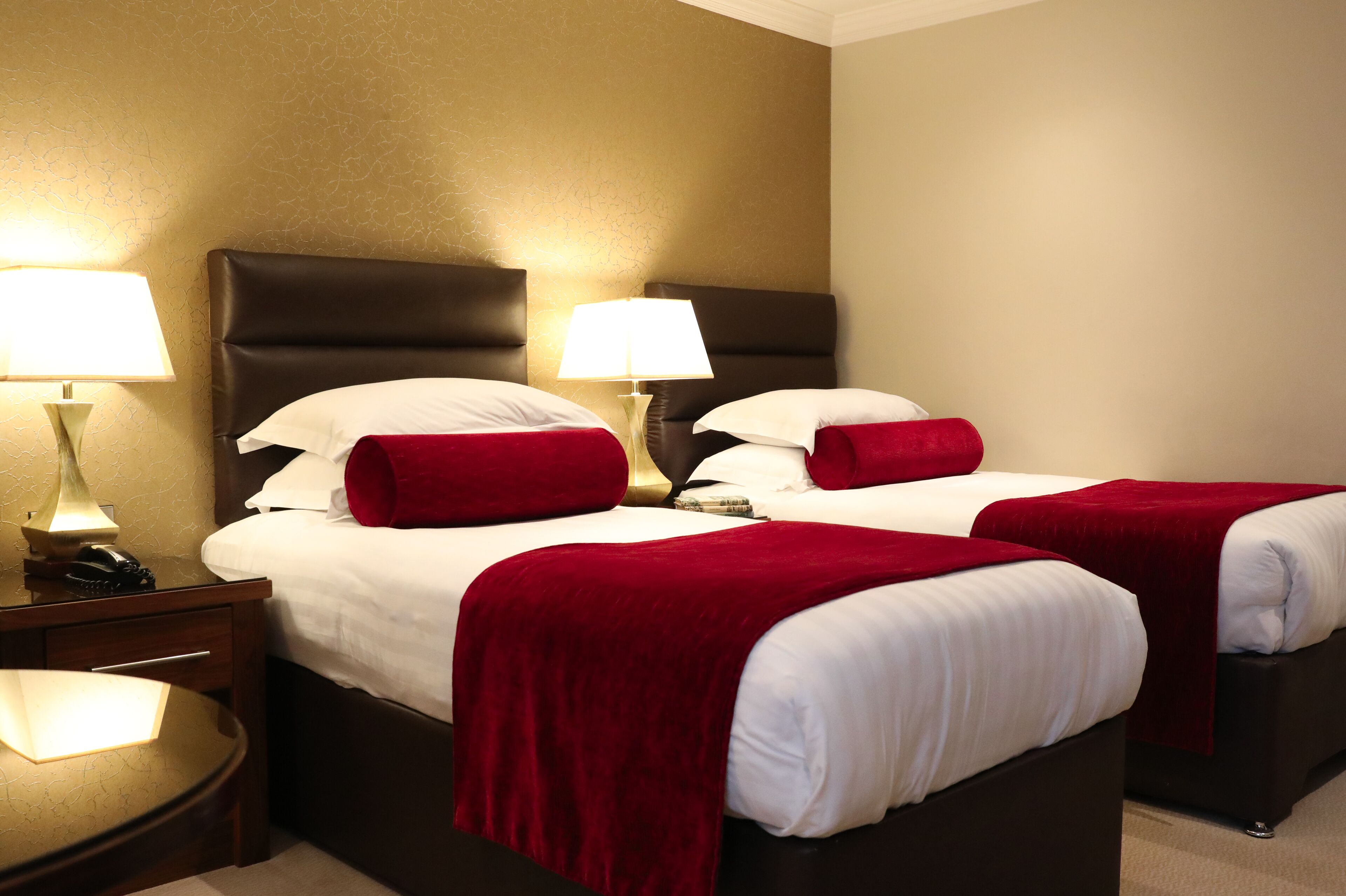 A hotel room with two beds, each with a red blanket, white pillows, and a lamp on a bedside table.