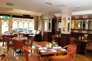 Un restaurante con mesas y sillas de madera, una chimenea y ventanas amplias.