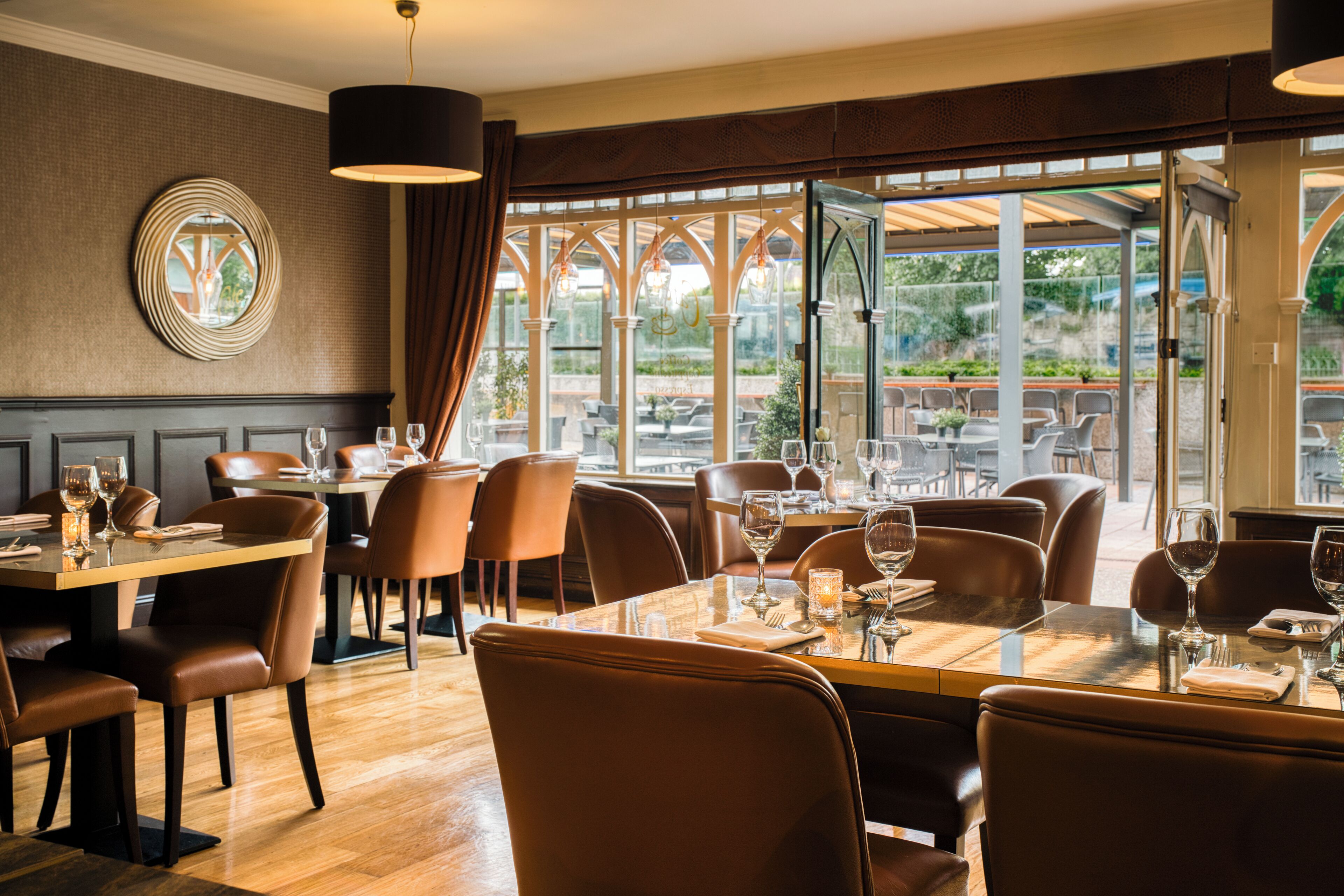 A restaurant with tables set for dining, chairs, and a view of the outdoors.