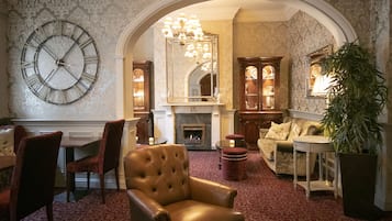 A room with a large clock, a fireplace, a sofa, and a dining area.