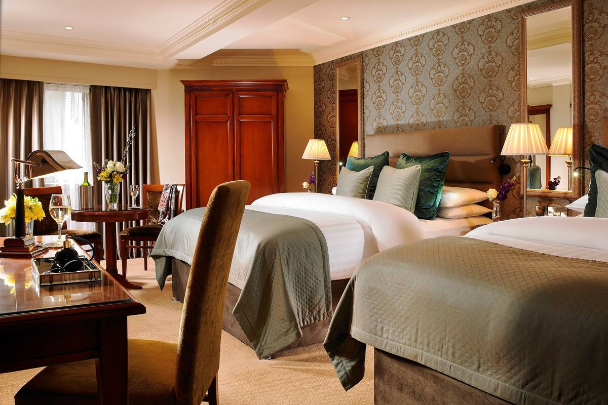 A hotel room with two beds, a desk, a chair, a dresser, and a large mirror.