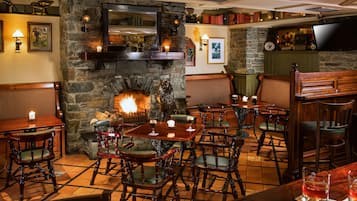 A cozy restaurant with stone walls, a fireplace, wooden furniture, and a television mounted on the wall.