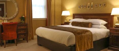 Habitación de hotel con una cama grande, un escritorio con silla, un espejo y una ventana con cortinas.