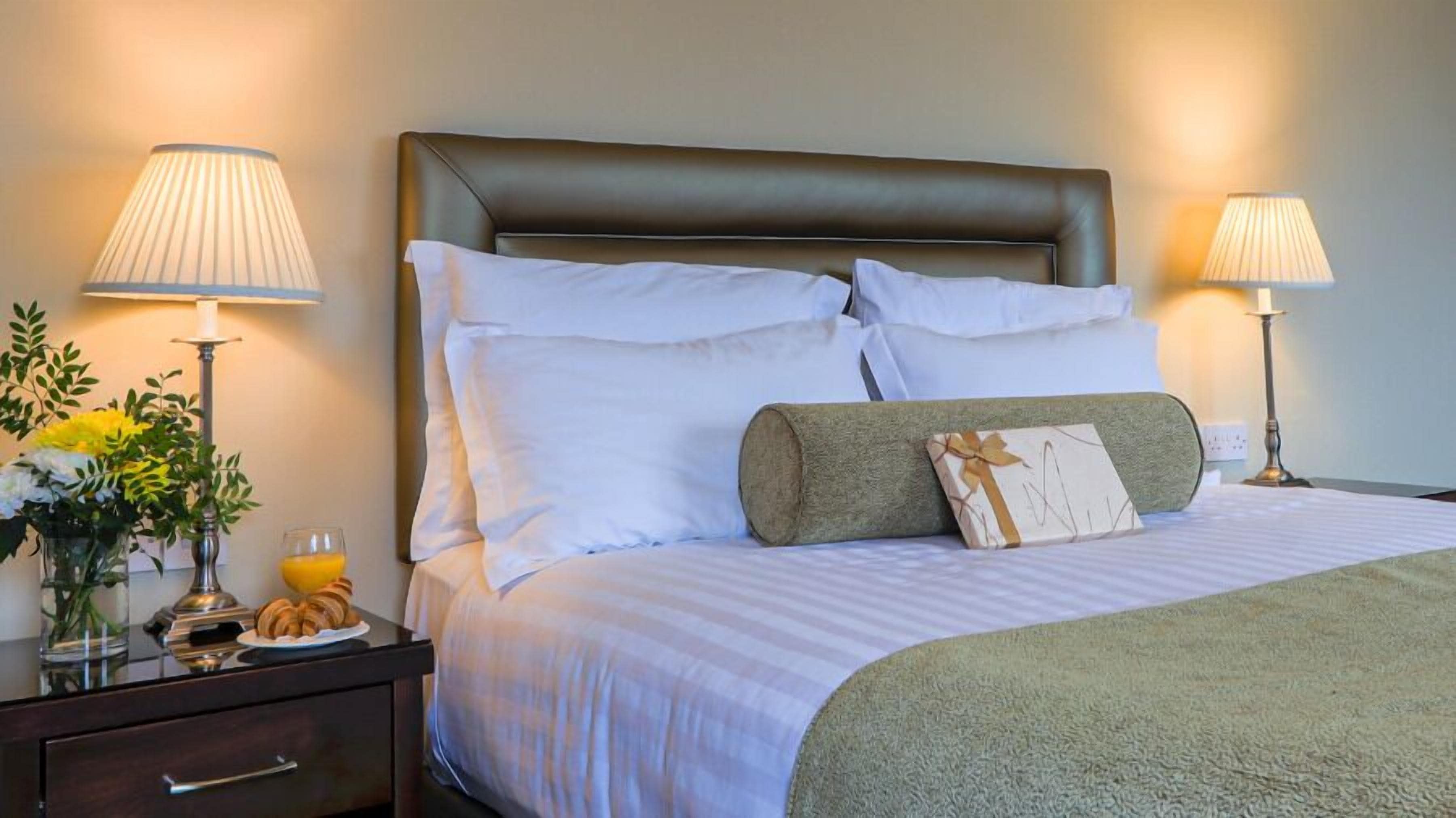 A neatly made bed with white linens and a brown headboard, flanked by two bedside lamps.