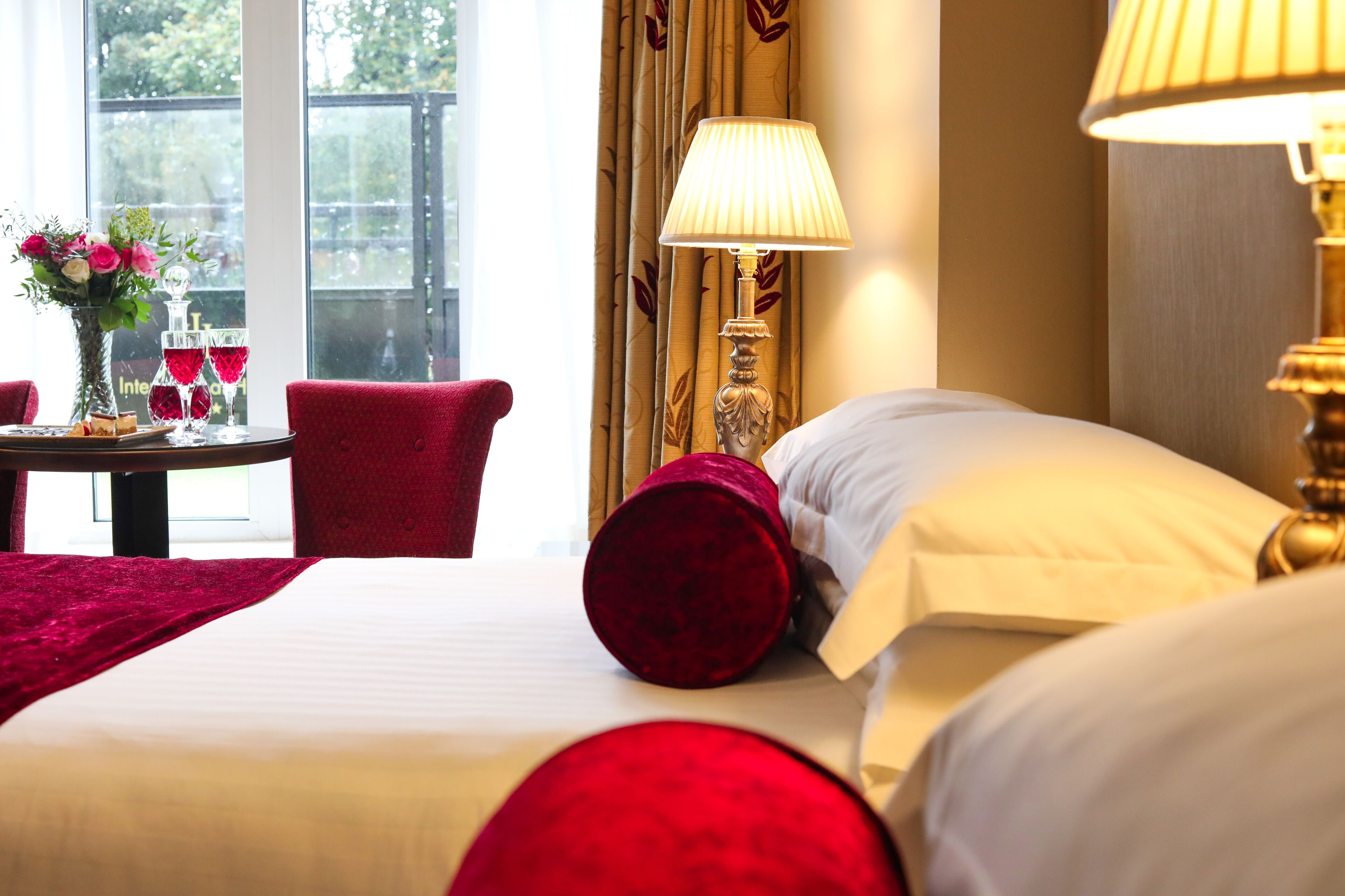 A hotel room with a bed, a table with a vase of flowers, and a window with curtains.
