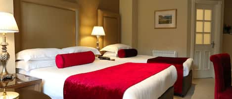 A hotel room with a large bed, two bedside lamps, a red throw pillow, a red chair, and a painting on the wall.