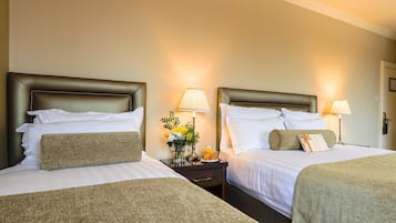Quarto de hotel com duas camas, cada uma com cabeceira, mesas de cabeceira com abajures e um vaso com flores.