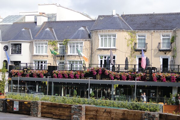 Un hotel con balcón decorado con flores y banderas, que presenta un estilo arquitectónico tradicional con numerosas ventanas y fachada de ladrillo.