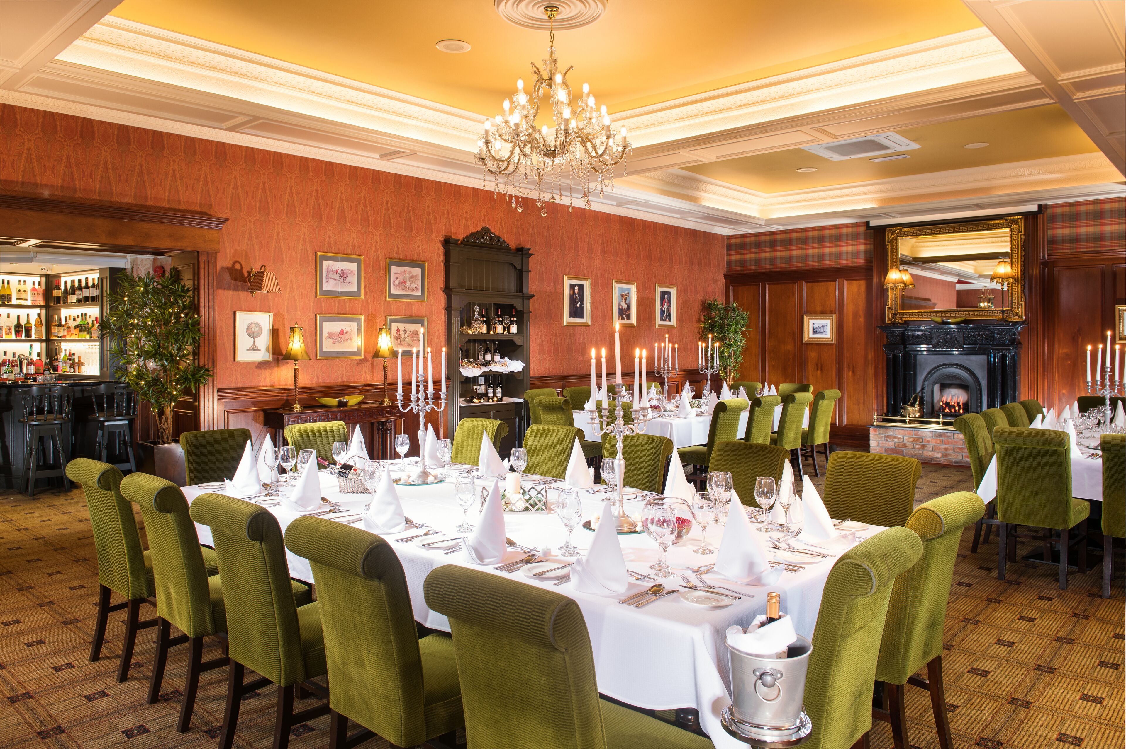 Une salle à manger élégante, avec des chaises recouvertes d’un tissu vert, des nappes blanches et des bougies.