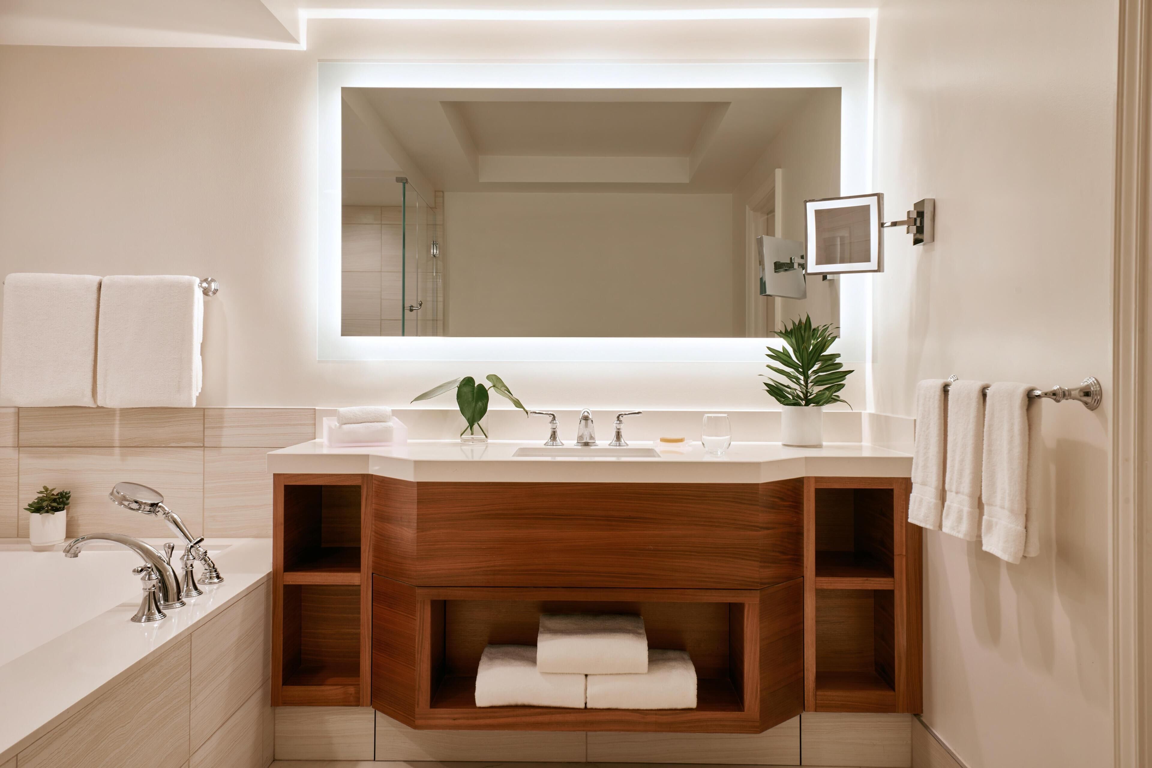 A modern bathroom with a large mirror, a bathtub, a vanity with a sink, and a potted plant.