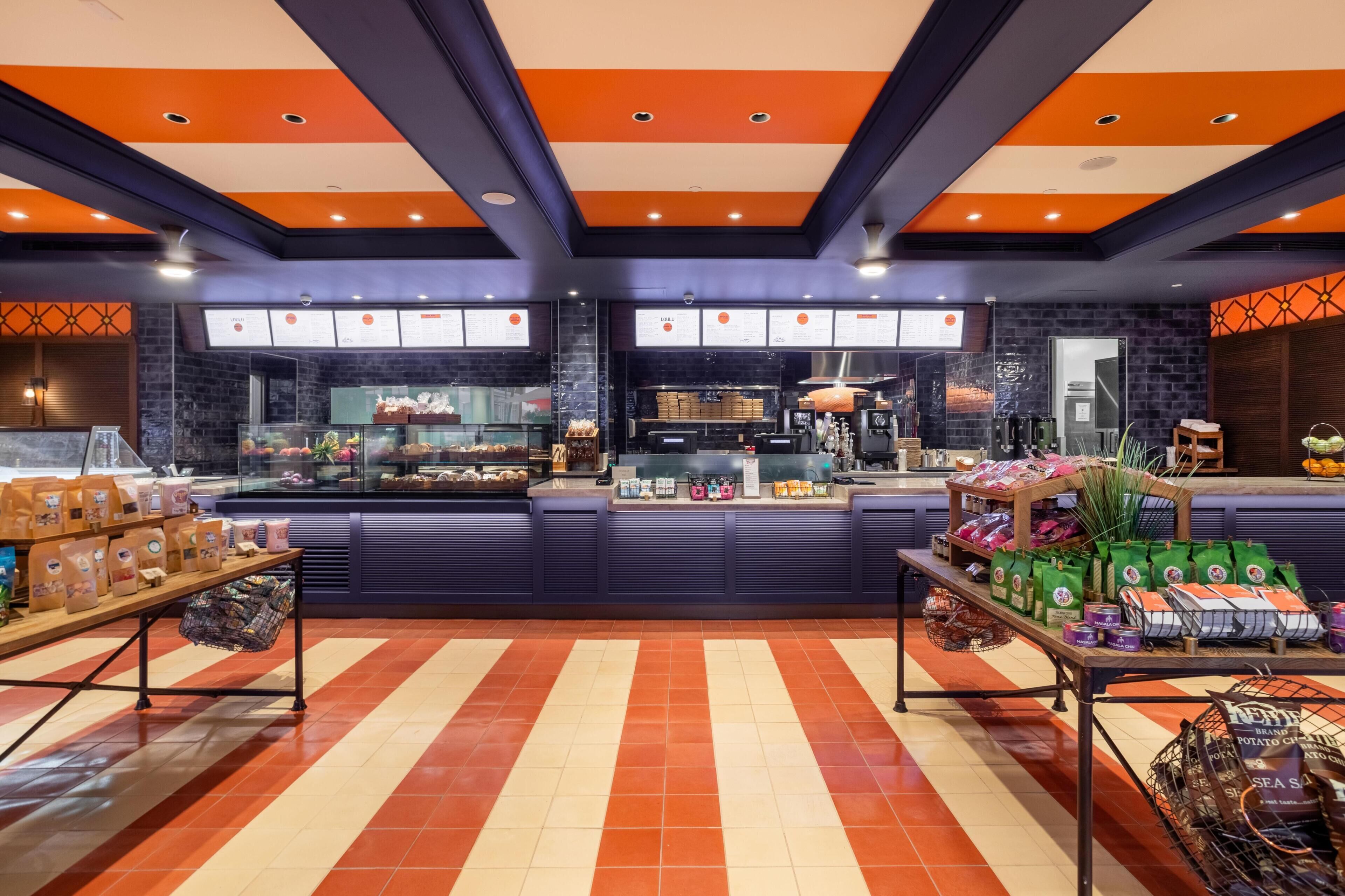 A bakery with a counter displaying baked goods, a seating area with tables, and a menu board.