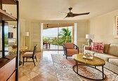 A spacious living room with a balcony, a ceiling fan, a sofa, a coffee table, and a dining area with a table and chairs.