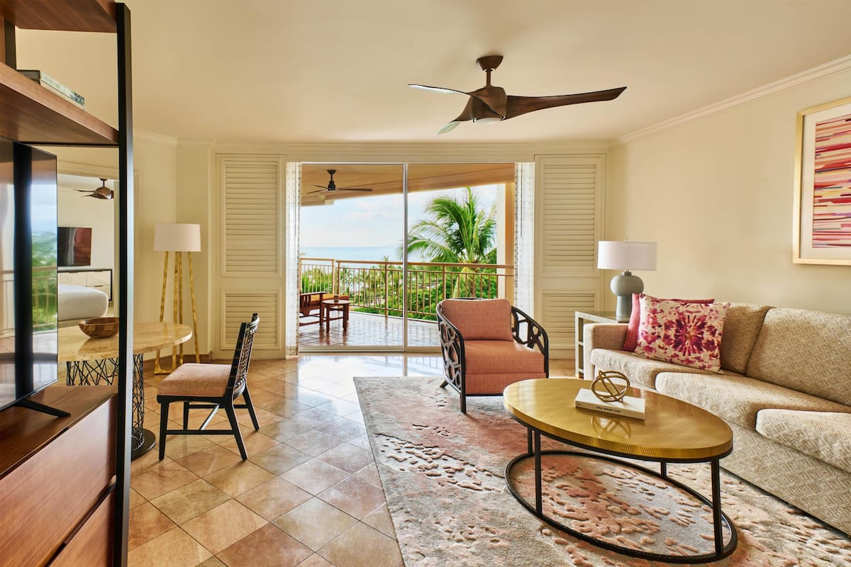 A spacious living room with a balcony, a ceiling fan, a sofa, a coffee table, and a dining area with a table and chairs.