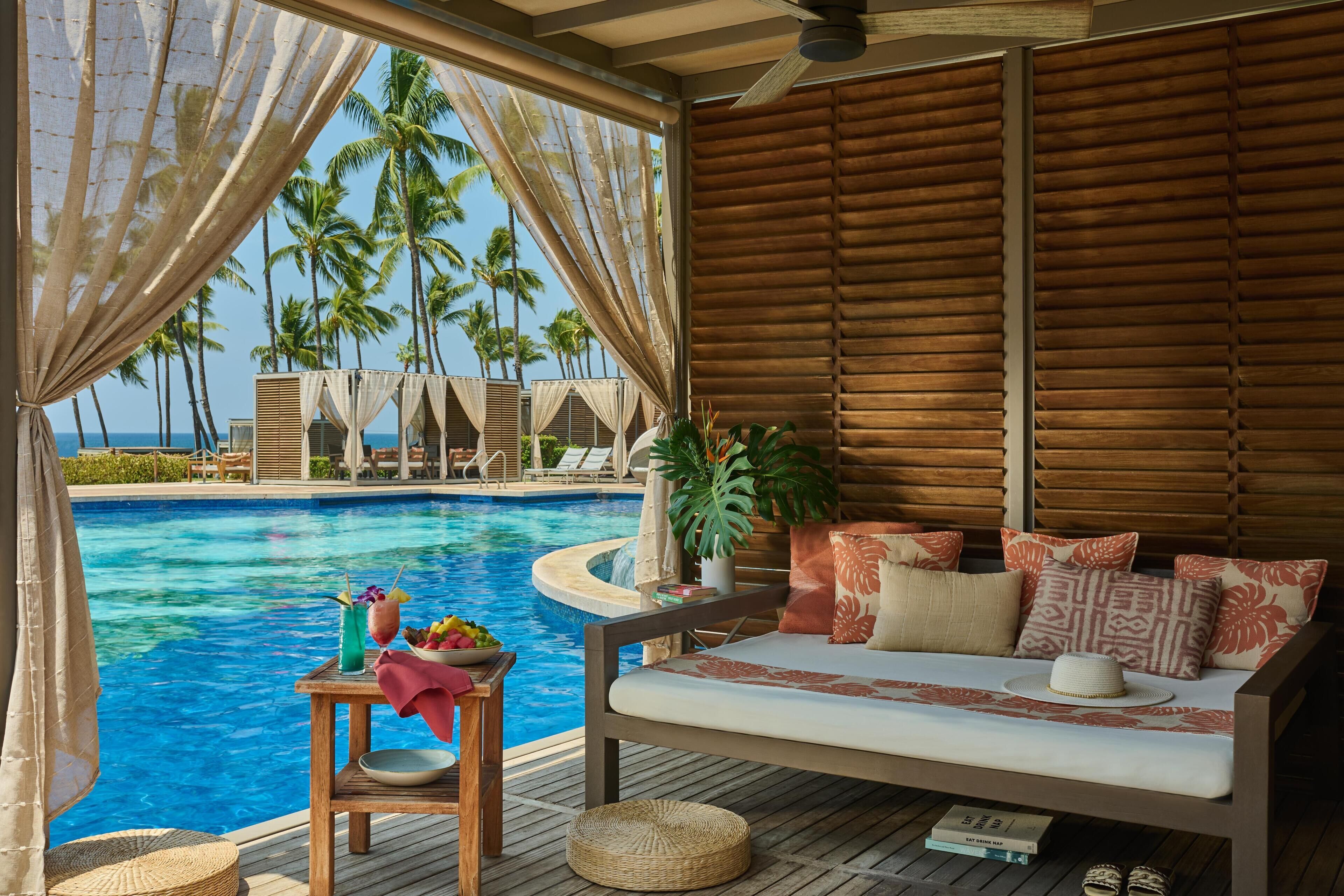 Een terras aan het zwembad met uitzicht op palmbomen, een houten dek en een comfortabele zithoek.