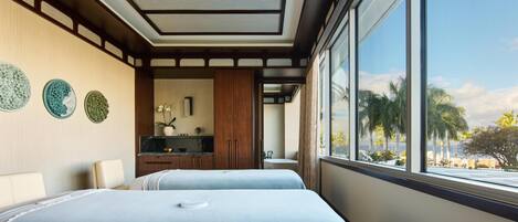 A hotel room with two beds, a kitchenette, and a large window with a view of palm trees.