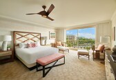 A hotel room with a large bed, a ceiling fan, a balcony with a view, and a desk with a lamp.
