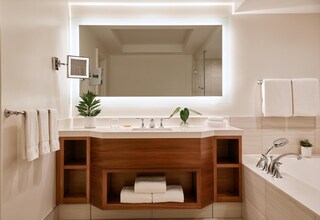 A modern bathroom with a large mirror, a wooden vanity, a bathtub, and a potted plant.