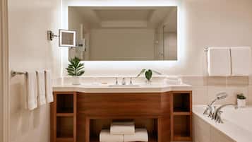 A modern bathroom with a large mirror, a wooden vanity, a bathtub, and a potted plant.