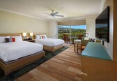 A hotel room with two beds, a desk, a chair, a TV, and a balcony with a view.