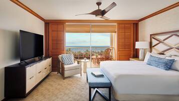 A hotel room with a large bed, a TV, a ceiling fan, a balcony with a view, and a desk with a lamp.