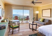 A hotel room with a bed, a desk, a chair, a sofa, a table, and a balcony with chairs.