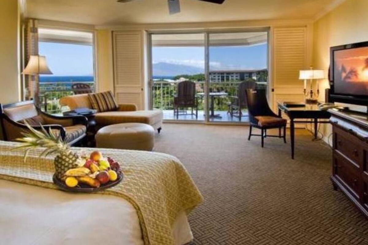 A hotel room with a bed, a desk, a chair, a television, and a balcony with a view.