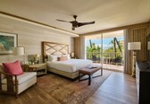 A hotel room with a bed, a chair, a desk, a ceiling fan, and a balcony with outdoor furniture.