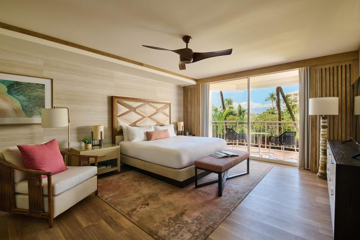 A hotel room with a bed, a chair, a desk, a ceiling fan, and a balcony with outdoor furniture.